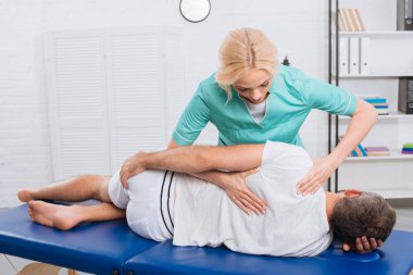 chiropractor massaging back on patient on massage table in hospital clipart