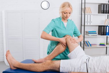 partial view of chiropractor massaging patients leg during appointment in clinic clipart
