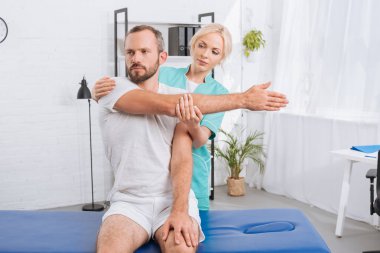 portrait of physiotherapist stretching mans arm in hospital clipart