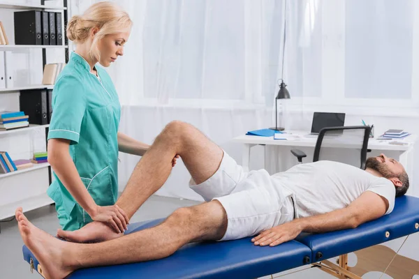 患者の診療所でのマッサージ テーブルの上に脚のマッサージを行う女性マッサージセラピスト — ストック写真