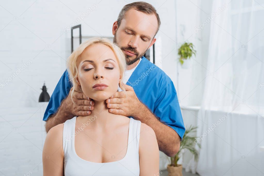 portrait of massage therapist massaging neck of young woman in clinic
