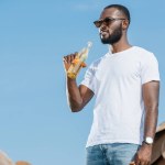Guapo afroamericano hombre bebiendo soda contra el cielo azul