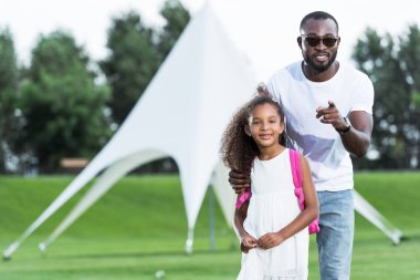 Afrikalı-Amerikalı babası okul çantası Park ile sevimli kızı kameraya gösteren