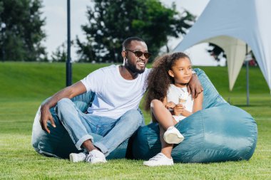 Afro-Amerikan baba ve kızı park ve uzak arıyor beanbag sandalye üzerinde oturan dondurma ile