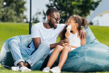 Afro-Amerikan baba ve kızı birbirlerinin beanbag sandalye Park tarih arıyorum dondurma ile gülümseyen