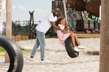 Afro-Amerikan baba ve kızı lastik salıncak eğlence parkı üzerinde