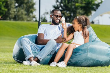 Afro-Amerikan kızı babası ile beanbag sandalye üzerinde otururken dondurma ile eğleniyor 