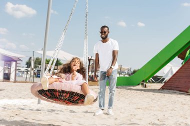 Afro-Amerikan kızı örümcek web yuva salıncak eğlence parkı üzerinde lolipop yemek 