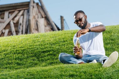 Afro-Amerikan yakışıklı soda şişesi yeşil tepe üzerinde açma