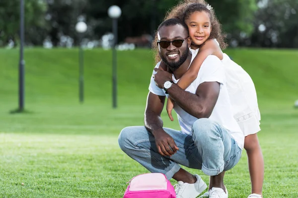 Афроамериканська Дочка Обіймає Батька Ззаду Парку Рожевий Мішок Траві — Безкоштовне стокове фото