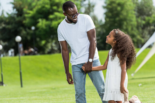 african american father and daughter holding hands and looking at each other in park