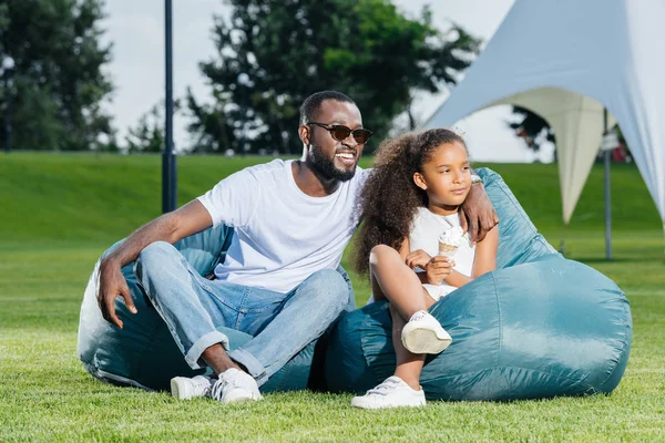 Afro-Amerikan baba ve kızı park ve uzak arıyor beanbag sandalye üzerinde oturan dondurma ile