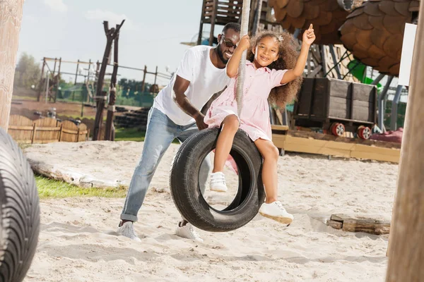 African American Father Pushing Daughter Tire Swing Amusement Park — Stock Photo, Image