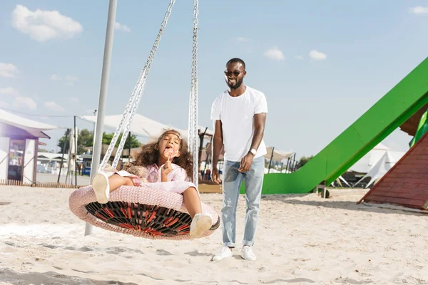 Afro-Amerikan kızı örümcek web yuva salıncak eğlence parkı üzerinde lolipop yemek 