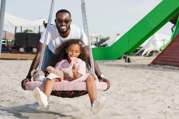 Sorridente Padre Afroamericano Spingendo Figlia Ragnatela Nido Altalena Con Lecca — Foto Stock