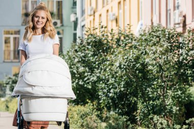 gülümseyen anne bebek arabası ile sokakta yürürken ve kameraya bakıyor