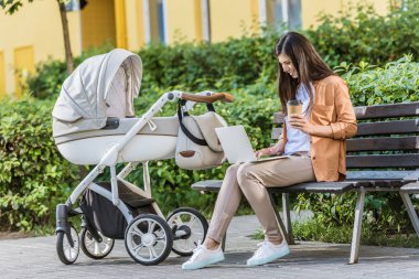 Bebek arabası Park yakınındaki bankta laptop ile çalışma ve kağıt bardak kahve tutarak serbest meslek