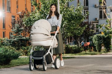 beautiful brunette mother walking with baby stroller on street clipart
