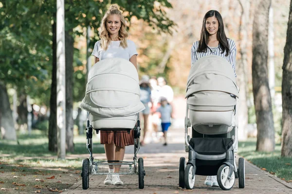 Mosolyogva Anyák Séta Parkban Látszó Fényképezőgép Babakocsik — Stock Fotó