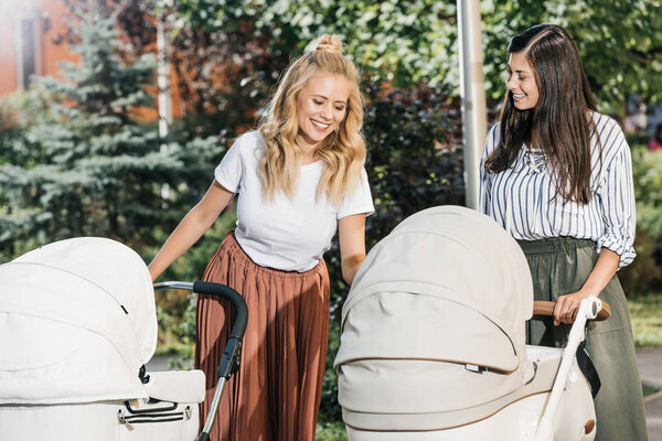 smiling mothers looking at baby strollers in park