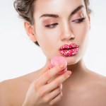 Attraktiva flicka med socker strössel på läppar hålla rosa macaron, isolerad på vit