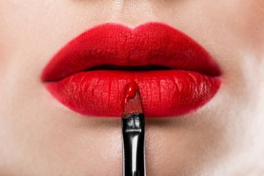 close up view of elegant woman applying red lipstick with cosmetic brush clipart