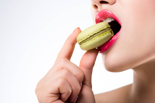 cropped view of woman biting green macaron, isolated on white