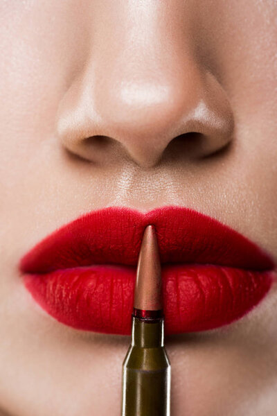 cropped view of girl holding bullet near red lips, isolated on grey