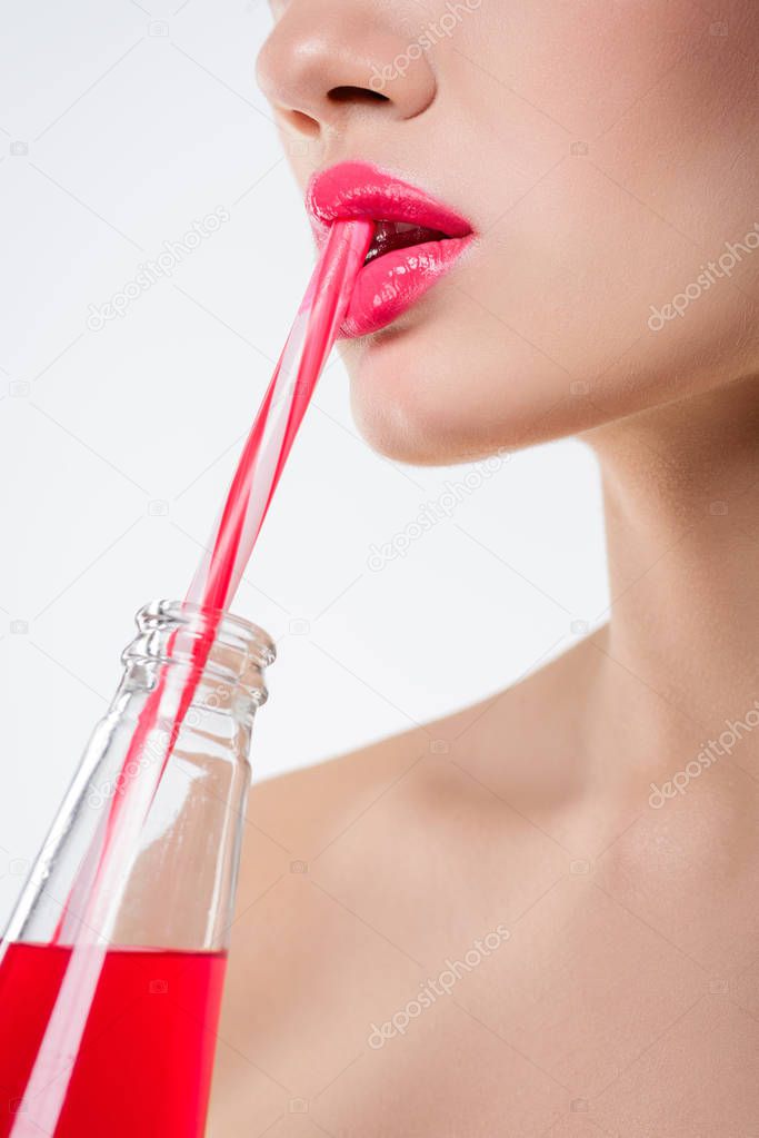 close up view of girl drinking pink beverage from bottle with straw, isolated on white