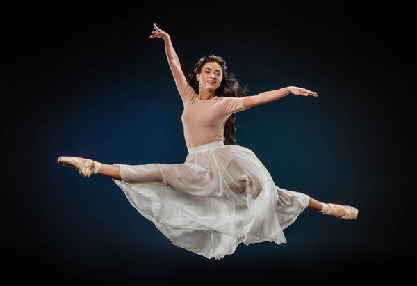 молодая балерина в элегантной одежде, прыгающая на темном фоне

