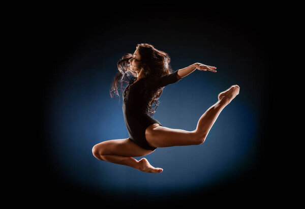 side view of beautiful ballerina in black bodysuit jumping on dark background