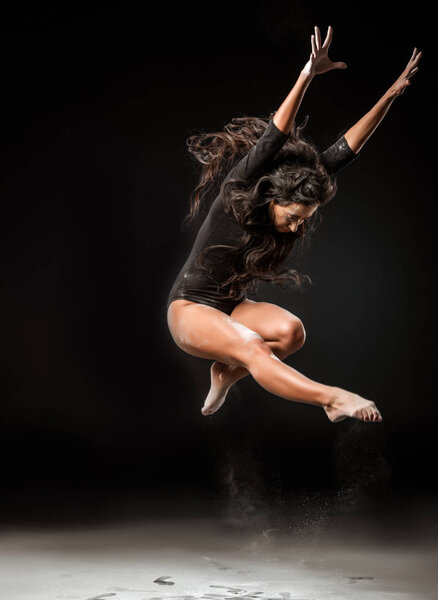 beautiful ballerina in black bodysuit jumping on dark background