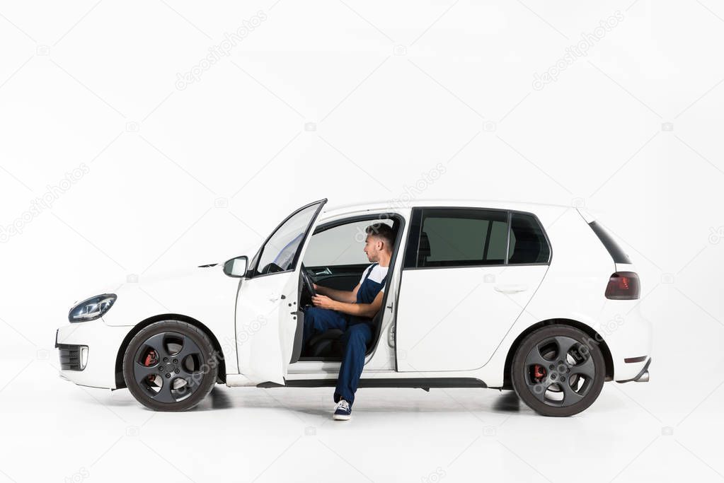 side view of handsome auto mechanic sitting in car on white