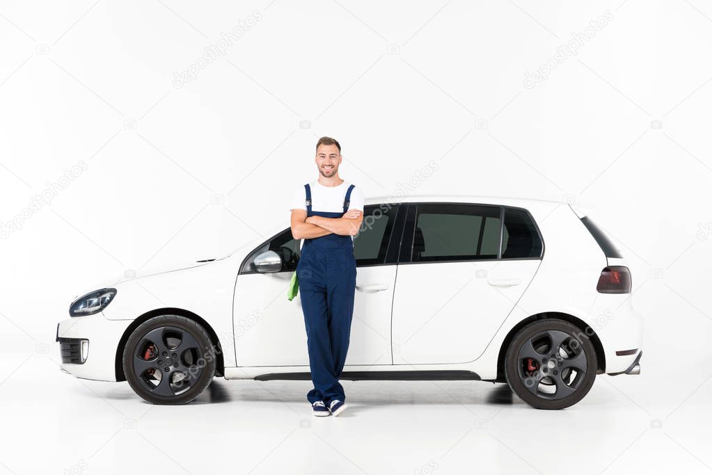 smiling handsome auto mechanic leaning on car with crossed arms on white