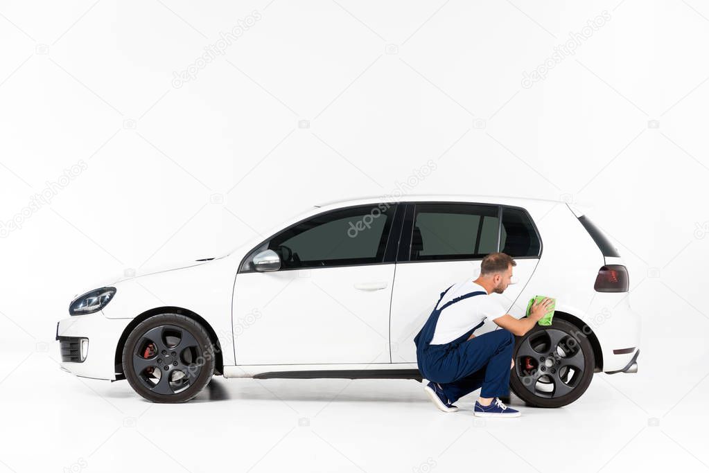 auto mechanic squatting and cleaning car after repairing on white