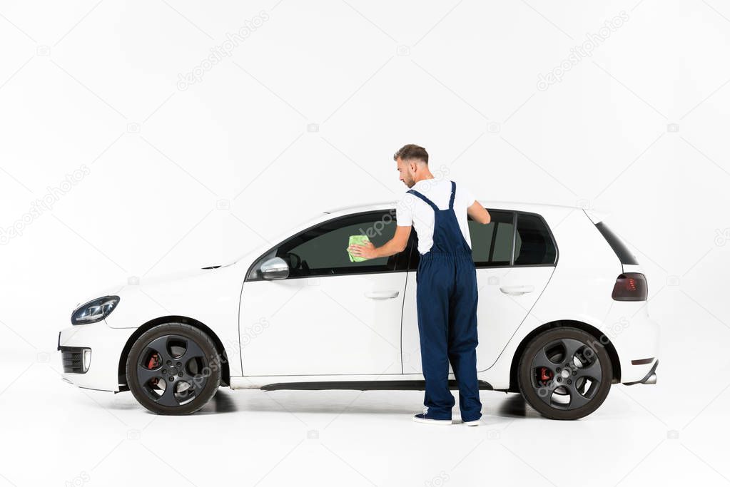 back view of auto mechanic cleaning car window after repairing on white