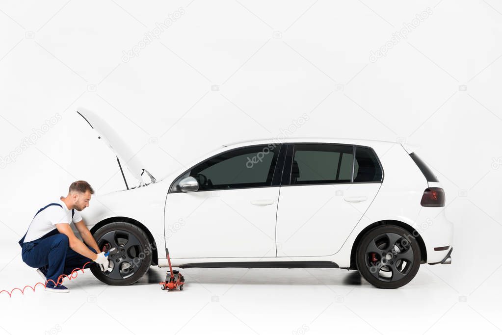 side view of auto mechanic inflating tire and checking air with gauge pressure on white