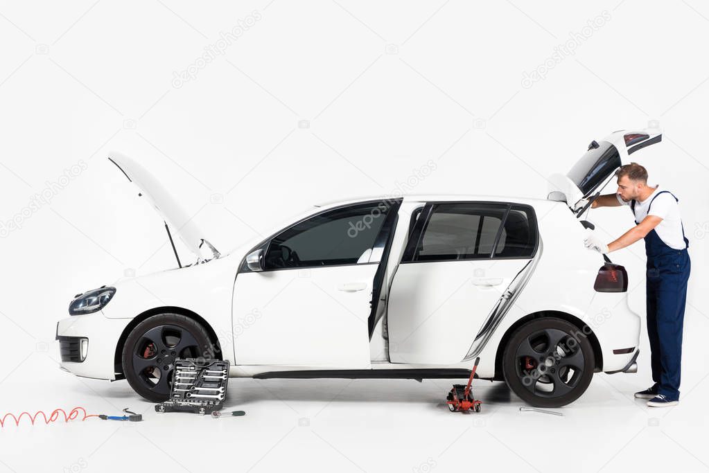 side view of handsome auto mechanic looking in open car trunk on white