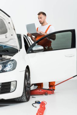 Dizüstü kırık araba beyaz izole yakın tutarak turuncu üniformalı yakışıklı otomatik mekanik