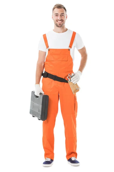 smiling handsome auto mechanic in orange uniform holding toolbox isolated on white