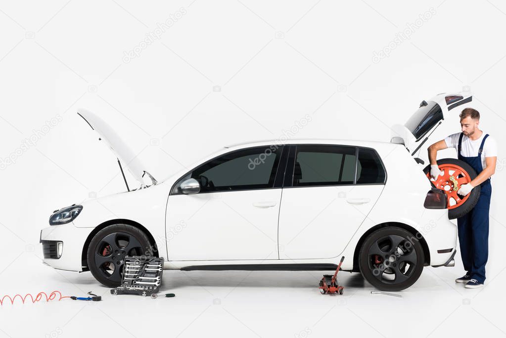 auto mechanic taking tire from car trunk on white