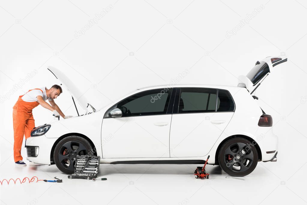 handsome auto mechanic repairing broken car on white