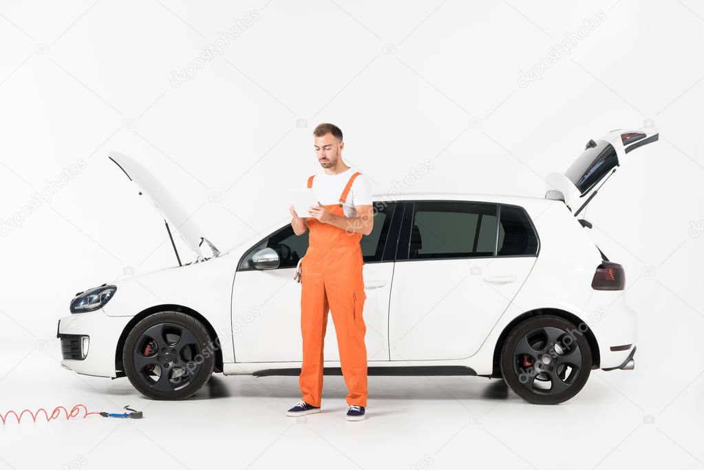 handsome auto mechanic using tablet near broken car on white