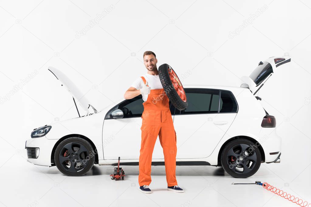 auto mechanic holding car tire and showing thumb up on white