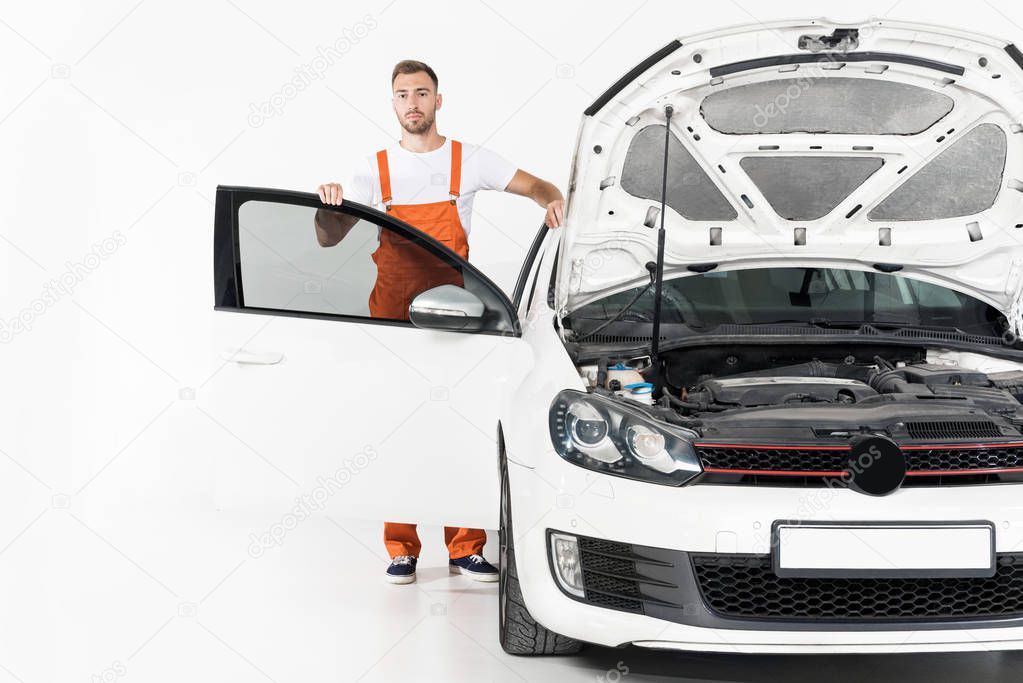 handsome auto mechanic standing near car with open hood and door on white