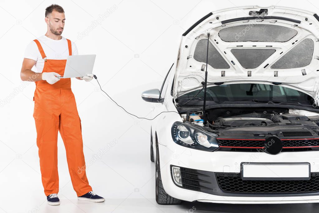 handsome auto mechanic checking broken car with laptop on white
