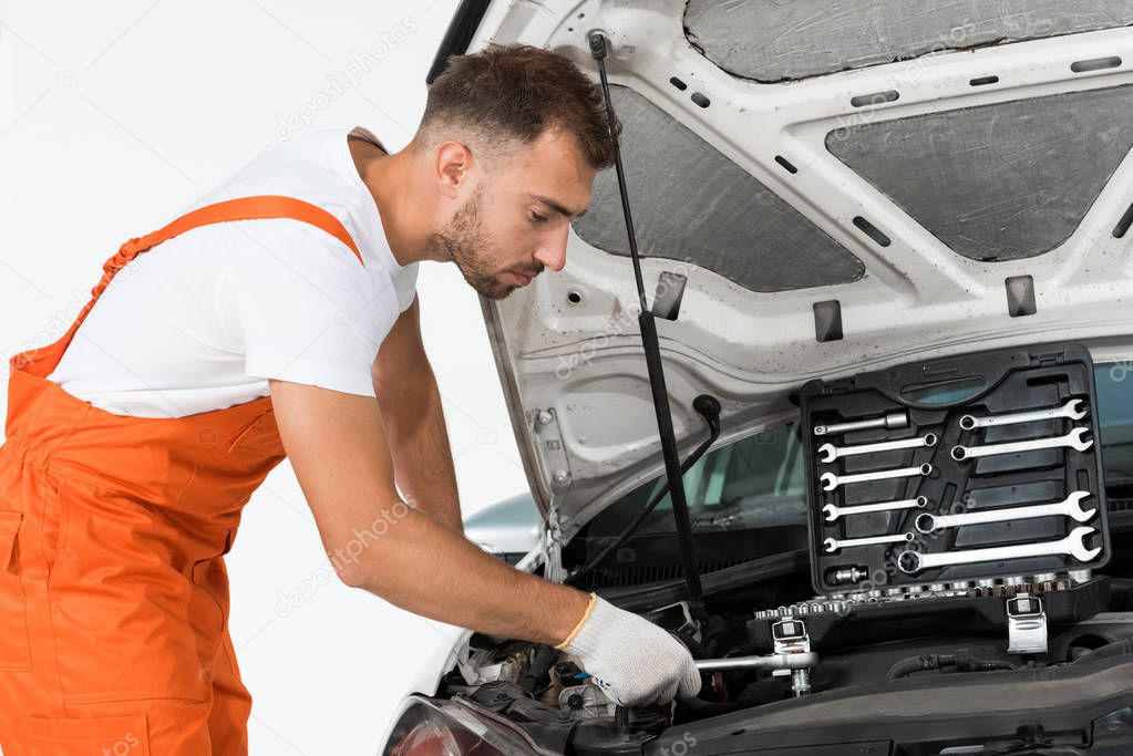 side view of handsome auto mechanic auto mechanic fixing car with wrench on white