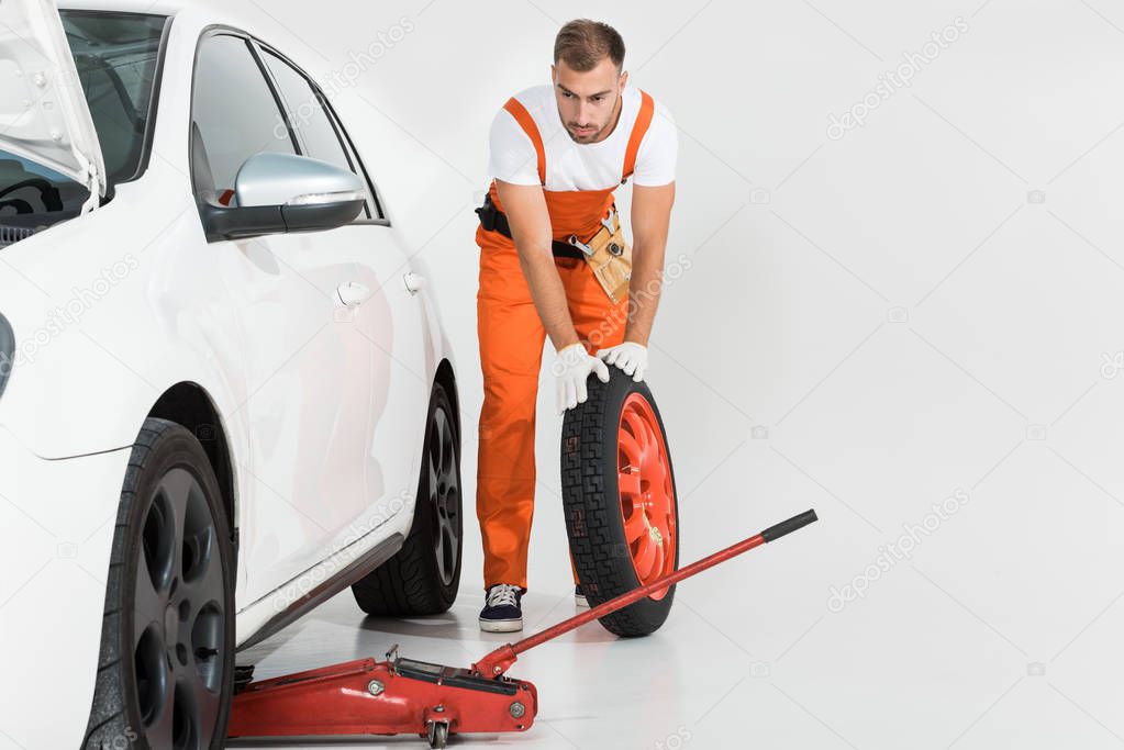 auto mechanic rolling tire to car on white