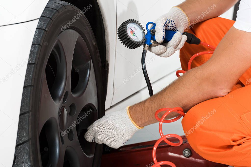 cropped image of auto mechanic inflating tire and checking air with gauge pressure