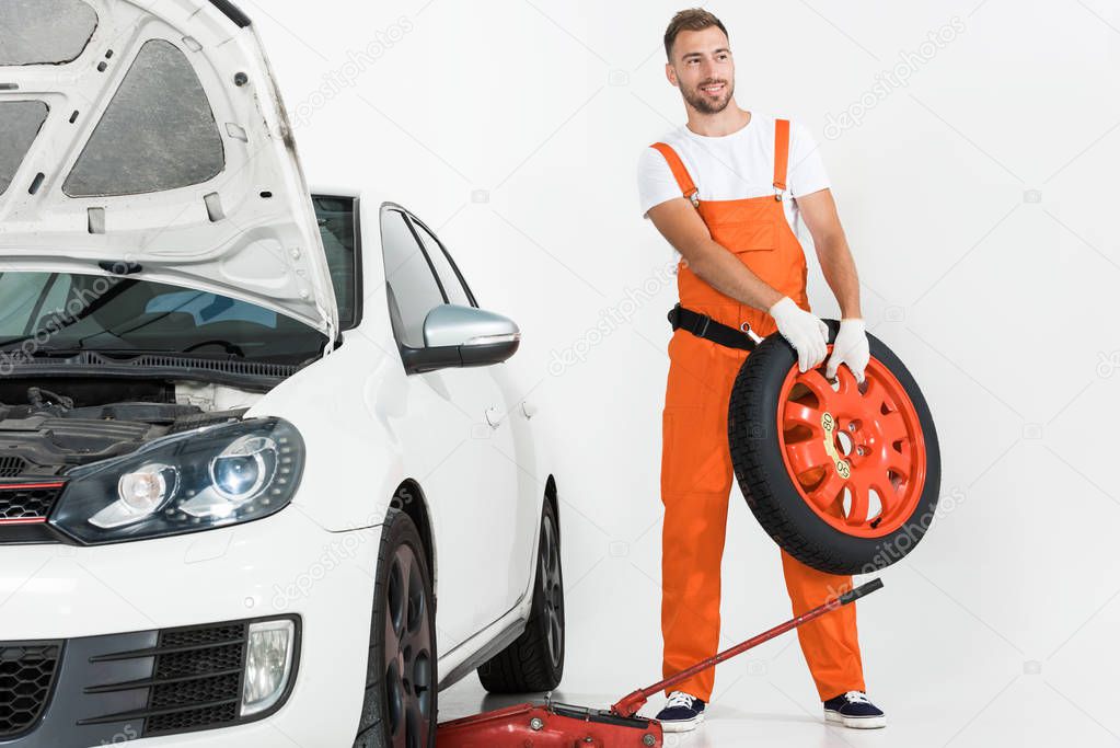 auto mechanic carrying car tire on white